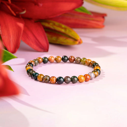 Quiet My Mind Ocean Jasper Bracelet with 6mm multicolored polished beads on a pink surface, surrounded by pink and red