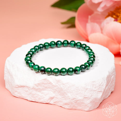 The Anxiety Bracelet 6mm in green pearls displayed on a white textured stone with pink background and a pink flower.