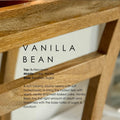 Vanilla Bean soy candle with white label and black text, placed on a wooden surface.
