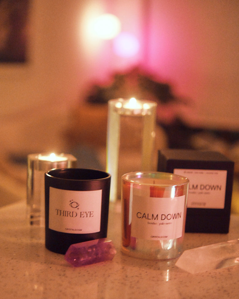 Third Eye Candle with black container, Calm Down Candle in clear glass jar, surrounded by crystals and lit candles.