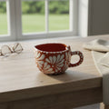 Talavera Heart Mug, hand-painted ceramic coffee cup with red and white floral design, placed on a wooden surface near a